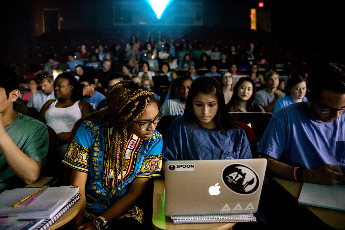 Two students look at a laptop during a class.
